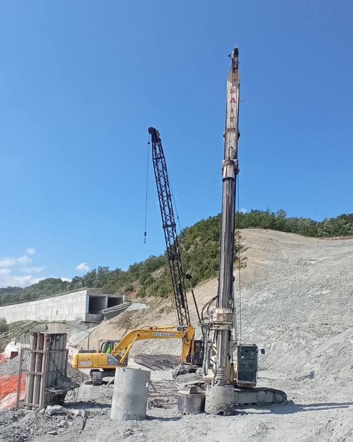 Escavatore giallo e perforatrice su cantiere in collina