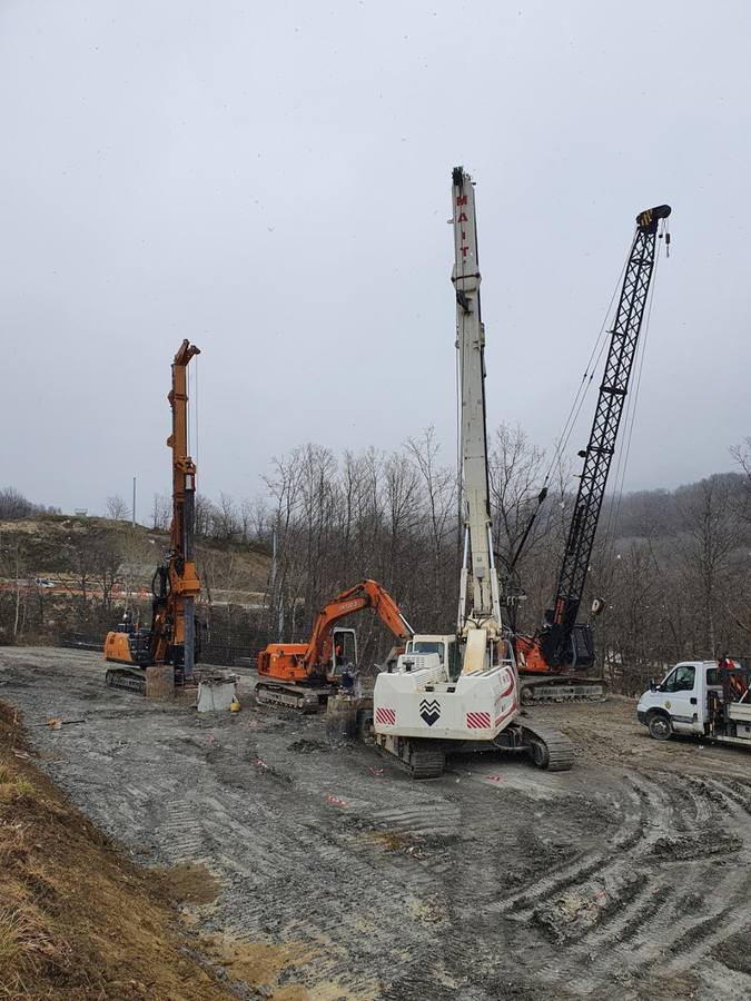Cantiere fangoso con perforatrice, escavatore e gru